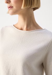 Beige sweater with a smooth texture, wide round neckline, and slightly dropped shoulders. Soft fabric and minimal seams.