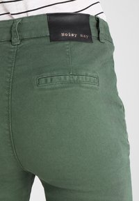 Zielone bawełniane spodnie o dopasowanym kroju, z czarną metką na pasku z napisem "Noisy May" oraz jedną tylną kieszenią.