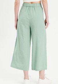 Pantalon vert clair, coupe large jambes, avec une ceinture élastique, fabriqué dans un tissu doux et léger. Texture lisse, coupe longueur cheville, sans poches.