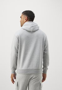 Felpa grigia con cappuccio, con polsini e orlo a coste, caratterizzata da una texture morbida. La vista posteriore mostra una vestibilità comoda e un design minimal.