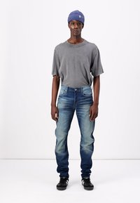 Grå, kortärmad t-shirt, ljusblå denimjeans, välsittande med blekningar, kombinerad med svarta sneakers och en blå stickad mössa.