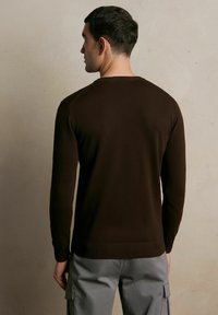 Brązowy sweter dzianinowy z okrągłym dekoltem, długimi rękawami i ribbanymi wykończeniami, połączony z jasnoszarymi spodniami cargo.