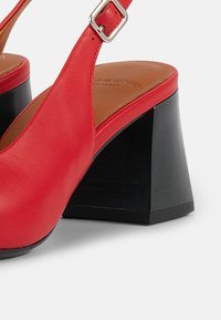Red leather high-heeled sandals with a wide black block heel and an ankle strap featuring a silver buckle, smooth texture, and open design.