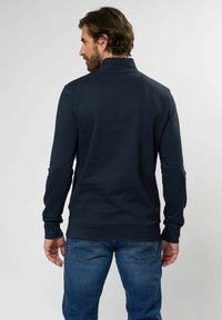 Polo de manga larga azul marino con cuello alto, hecho de tela suave; combinado con jeans de mezclilla azul claro con bolsillos traseros.