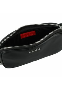 Borsetta in pelle nera con hardware in argento e chiusura a zip. Presenta un'etichetta di marca rossa all'interno, che mette in evidenza un design elegante e una texture liscia.