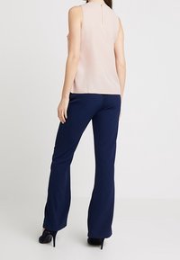 Rukávů prostá světle růžová halenka se zapínáním na zádech, doplněná tmavě modrými širokými kalhotami z hladké tkaniny pro elegantní vzhled.