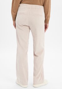 Pantalones de corduroy beige claro con pierna recta, cinturilla elástica y bolsillos traseros, que presentan una textura acanalada y un ajuste relajado.