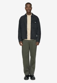 Men's black denim jacket with a chest pocket, cream sweater underneath, olive green pants, and black chunky boots, on a plain white background.