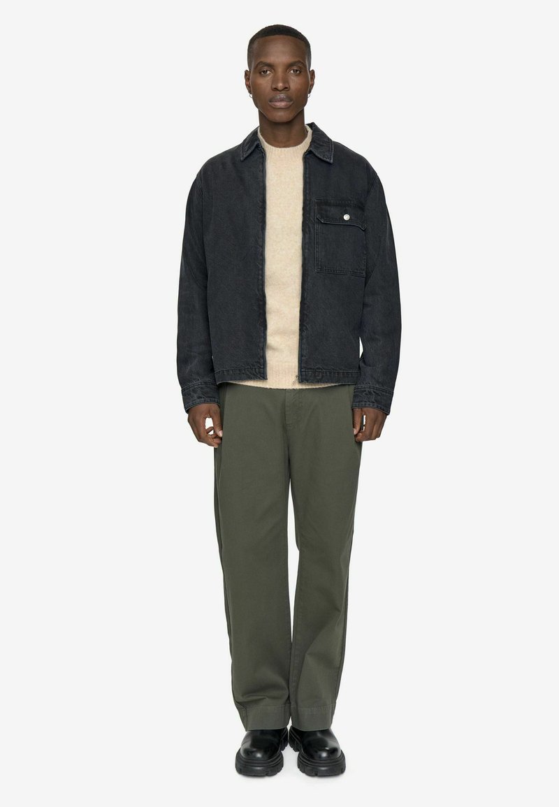 Men's black denim jacket with a chest pocket, cream sweater underneath, olive green pants, and black chunky boots, on a plain white background.