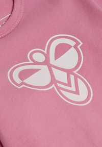 Rosa bomullströja med en stor vit fjärilsgrafik. Designen har geometriska former som betonar kurvor och vinklar i vingarna.