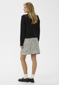 Svart tröja, rutigt kjol i svart och vitt, platta svarta skor, beige strumpor. Slät textur, figurnära design, knälång kjol.