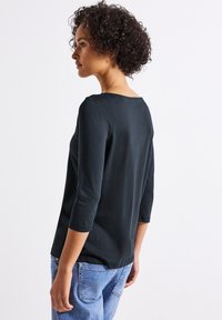 Top nero a tre quarti con scollo rotondo, realizzato in tessuto morbido, abbinato a jeans in denim blu chiaro. Design minimalista senza decorazioni.