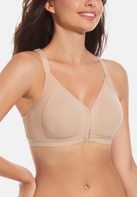 Sostenedor de copa suave beige con un diseño de cuello en V, costuras en melocotón contrastantes, tirantes ajustables y banda elástica sin costuras en la parte inferior.