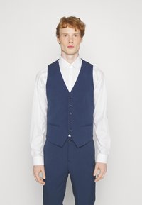Marineblaues Weste mit tailliertem Schnitt, fünf Knöpfen und zwei Seitentaschen, kombiniert mit einem weißen Hemd. Glatte Textur, klares Design.