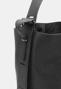 Borsa a tote in pelle nera con una texture a granuli, dotata di una maniglia larga, di una tracolla regolabile e dettagli in metallo.