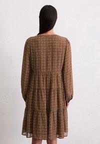 Braunes Kleid mit weißem Blättermuster, langen Ärmeln und gestuftem Rüschendesign, aus leichtem Material, mit rundem Ausschnitt.