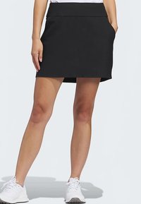 Falda deportiva negra con textura suave, con una cinturilla ancha y bolsillos laterales, combinada con zapatillas blancas para un contraste.