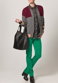 Gebreide cardigan in grijs met bordeauxaccenten, zwarte overhemd met kraag, groene broek en zwarte leren handtas. Zwarte haklaarzen maken de look compleet.