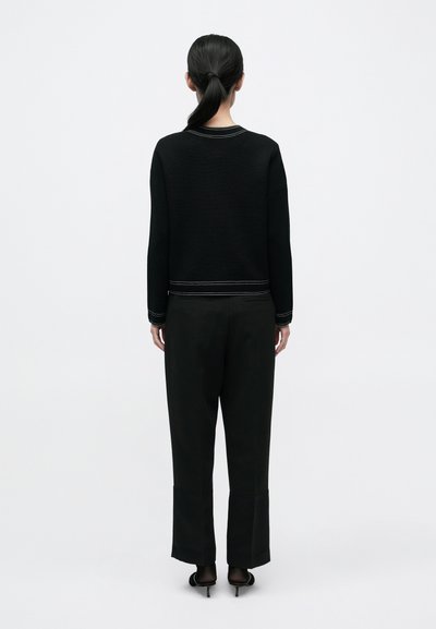 Fekete kötött pulóver rövidített fazonnal és kontrasztos varrással, laza fekete nadrággal és magassarkú szandállal párosítva. Egyszerű és minimalista dizájn.
