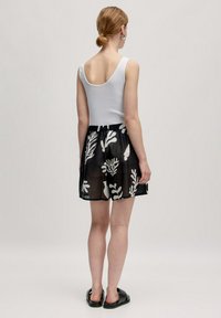 Débardeur blanc avec un décolleté profond dans le dos, associé à une jupe noire transparente ornée de motifs de plantes blancs et d'une taille élastique. Sandales noires.