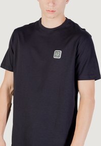 T-shirt in cotone nero con scollatura rotonda e maniche corte, dotato di un piccolo logo ricamato in un quadrato sulla parte sinistra del petto.