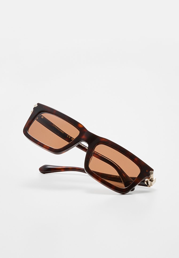 Lunettes de soleil en écaille de tortue avec des verres marron, de forme rectangulaire, avec de subtils accents métalliques et une monture épaisse offrant une apparence robuste.
