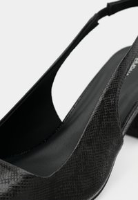 Μαύρο παπούτσι με λουράκι στην πλάτη, με επάνω μέρος από υφή ψεύτικου δέρματος, ανοιχτή πλευρική σχεδίαση και χαμηλό τακούνι τύπου block. Λείο εσωτερικό επένδυση.