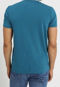 Teal lyhythihainen t-paita, joka on valmistettu sileästä kankaasta ja jossa on pyöreä pääntie sekä suora helma. Yhdistettynä sinisiin farkkuihin.