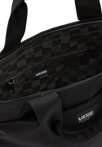 Czarna torba na ramię Vans z wnętrzem w kratkę, kieszenią na zamek oraz naszywką z logo z przodu zewnętrznej kieszeni.