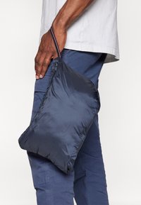 Granatowa, lekka, pikowana saszetka z suwakiem i pętlą do trzymania, idealna do kompaktowego przechowywania. Gładka, błyszcząca faktura.