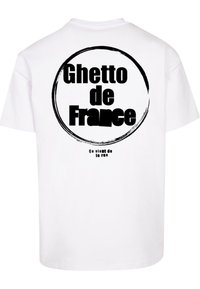 Balta 100% medvilnės marškinėliai su dideliu juodu apvaliu grafiniu išdėstymu su tekstu "Ghetto de France" ant nugaros ir mažesniu tekstu "Ça vient de la rue."