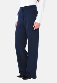 Pantaloni eleganti blu navy con un design fluido, realizzati in un tessuto liscio con chiusura a bottone e tasche frontali.