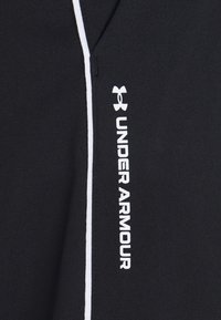 Svart atletisk tyg med vita accentlinjer och "UNDER ARMOUR"-logotyp i vitt. Har en slät yta och en åtsittande design.