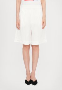 Shorts blancs, arrivant aux genoux, fabriqués en tissu léger avec une taille élastique, présentant une texture lisse et un design d'ourlet simple.