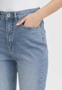 Jeans a vita alta di colore azzurro chiaro con una vestibilità slim, dotati di un bottone visibile, una cerniera nascosta e tasche. Tessuto denim testurizzato con una finitura sbiadita.