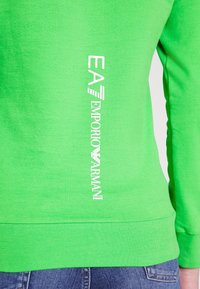 Felpa verde in cotone con scollo rotondo e polsini a coste, con la scritta bianca "EA7 Emporio Armani" sul lato sinistro.