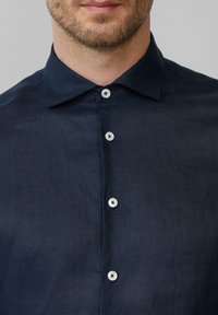 Navyblauwe button-up shirt gemaakt van een lichte, gestructureerde stof; beschikt over een spread collar en witte plastic knopen aan de voorkant.