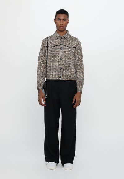 Cropped, patterned jacket with buttons, in beige, brown, and red hues. Paired with tailored black trousers and white sneakers.