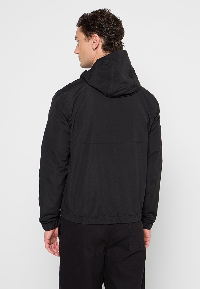 Veste noire à capuche avec fermeture éclair à l'avant, poignets élastiques et ourlet resserré. Texture lisse avec un design simple et minimal.