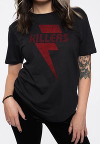 Black t-shirt featuring red "KILLERS" text and a lightning bolt graphic. Made of soft fabric with a loose fit, short sleeves, and round neckline.