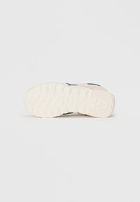 Suola bianca di una sneaker caratterizzata da tracce circolari e lineari, con il nome del marchio delicatamente impresso vicino al tallone.