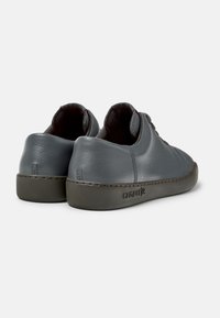 Sneaker in pelle grigia con una texture liscia, design a profilo basso e suole in gomma. Presenta dettagli cuciti e il marchio sul lato.