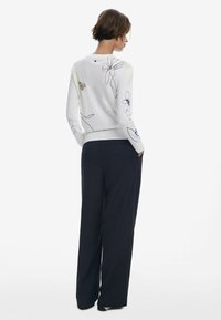 Maglione bianco con ricami floreali colorati, scollatura rotonda e orlo a costine, abbinato a pantaloni blu navy larghi.