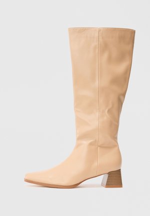 Botas de caña alta beige, hechas de un material sintético suave, con punta cuadrada y un tacón ancho con rayas horizontales que aportan textura.