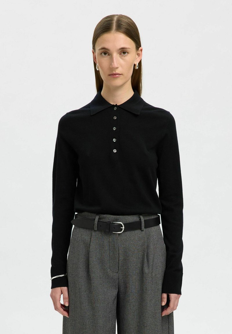 Maglione polo nero a maniche lunghe con colletto e sei bottoni frontali. Abbinato a pantaloni grigi e una cintura nera con fibbia in argento.