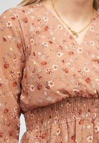 Robe florale de couleur rose poussiéreux, dotée d'un décolleté en V, d'une taille smockée et de petites fleurs blanches et rouges sur l'ensemble du tissu.