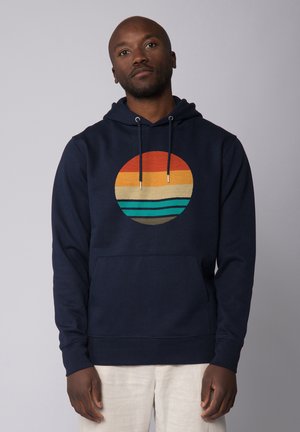 Marineblauwe hoodie met een cirkelvormige grafiek met horizontale strepen in oranje, geel en teal. Voorzien van een kangoeroezak en een trekkoordkap.