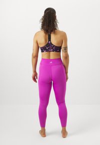 Reggiseno sportivo nero con motivo floreale, abbinato a leggings aderenti rosa brillante, che mostrano una texture liscia e elastica con un design a vita alta.