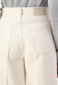 Bijele traperice širokih nogavica, s dva stražnja džepa i sivom oznakom Calvin Klein na struku. Glatka tekstura.