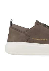 Sneaker in pelle marrone con suola in gomma bianca, caratterizzati da cuciture sottili, un logo dorato e una texture liscia. Design leggero.
